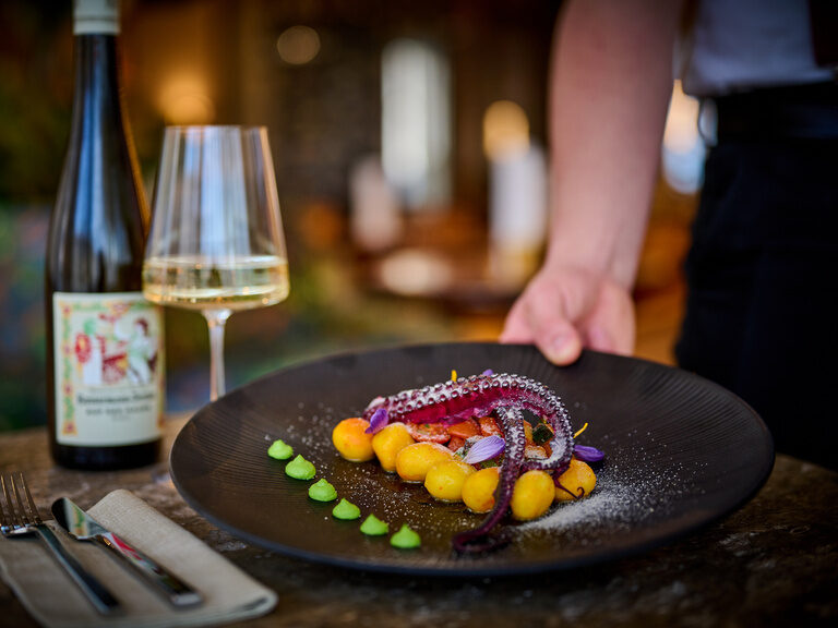 Ein Teller mit Oktopus wird gerade von einem Kellner serviert, ein Glas Wein steht bereits auf dem Tisch. Ein Teller mit Oktopus wird gerade von einem Kellner serviert, ein Glas Wein steht bereits auf dem Tisch.