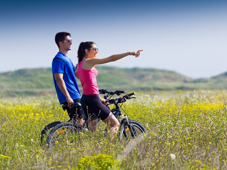 Ein junges Paar auf Fahrrädern bei einem Stopp auf einer Wiese. Ein junges Paar auf Fahrrädern bei einem Stopp auf einer Wiese.