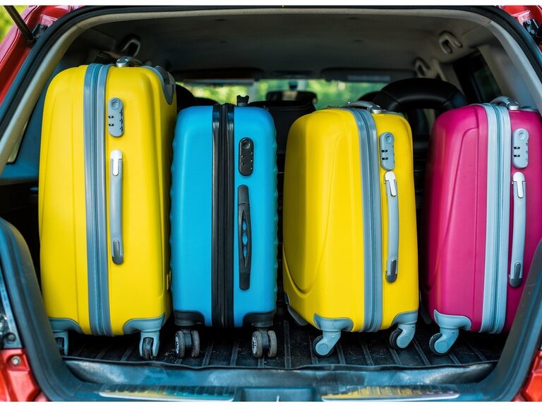 Blick in den Kofferraum eines Autos, in dem viele verschiedene bunte Koffer liegen