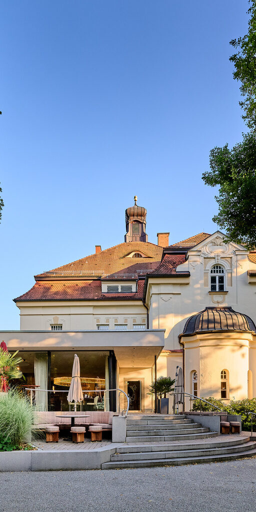 Blick von außen auf die Glasfront des Restaurant ASAM in Straubing, umgeben von üppiger grüner Bepflanzung. Blick von außen auf die Glasfront des Restaurant ASAM in Straubing, umgeben von üppiger grüner Bepflanzung.