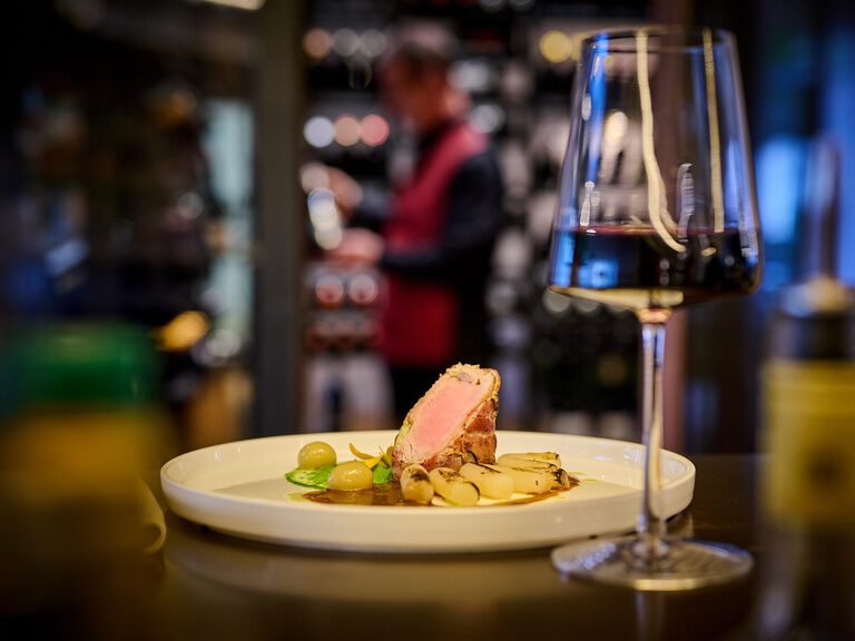 Ein fein angerichteter Telle rund ein Glas Rotwein im Restaurant ASAM, im Hintergrund der begehbare Weinschrank. Ein fein angerichteter Telle rund ein Glas Rotwein im Restaurant ASAM, im Hintergrund der begehbare Weinschrank.