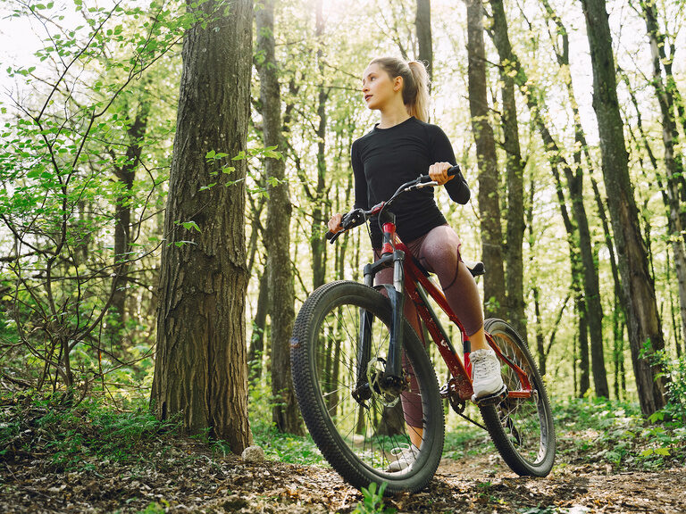 Eine sportliche Frau ist mit ihrem Fahrrad in einem Waldstück unterwegs.