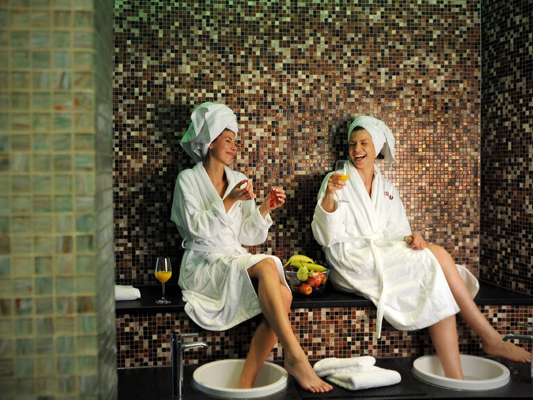 Zwei Freundinnen geniessen die Wellnessbehandlungen im Wellnessbereich mit einem Glas Sekt und guter Laune.