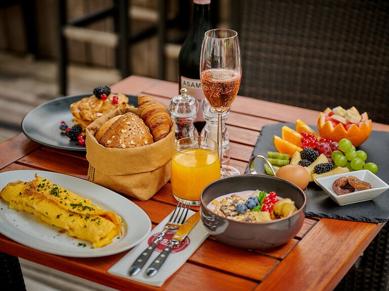 Frühstück im Hotel ASAM in Straubing: üppig gedeckter Tisch vom Buffet für Hotelgäste und externe Besucher. Junge Frau schaut in den Wald während Sie auf dem Fahrrad Pause macht.
